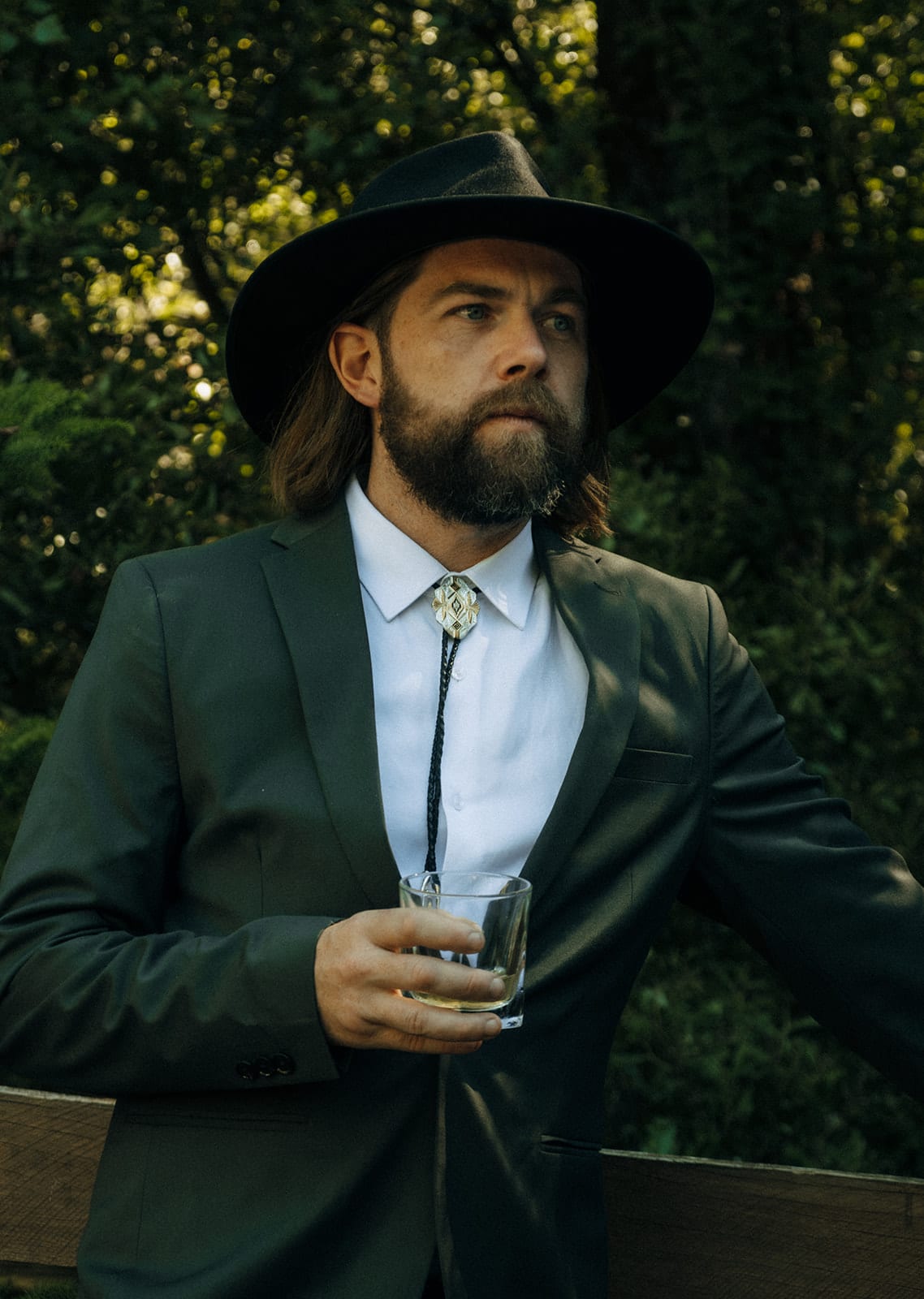 Todd in a wide-brimmed hat leaning on a timber fence in the shade