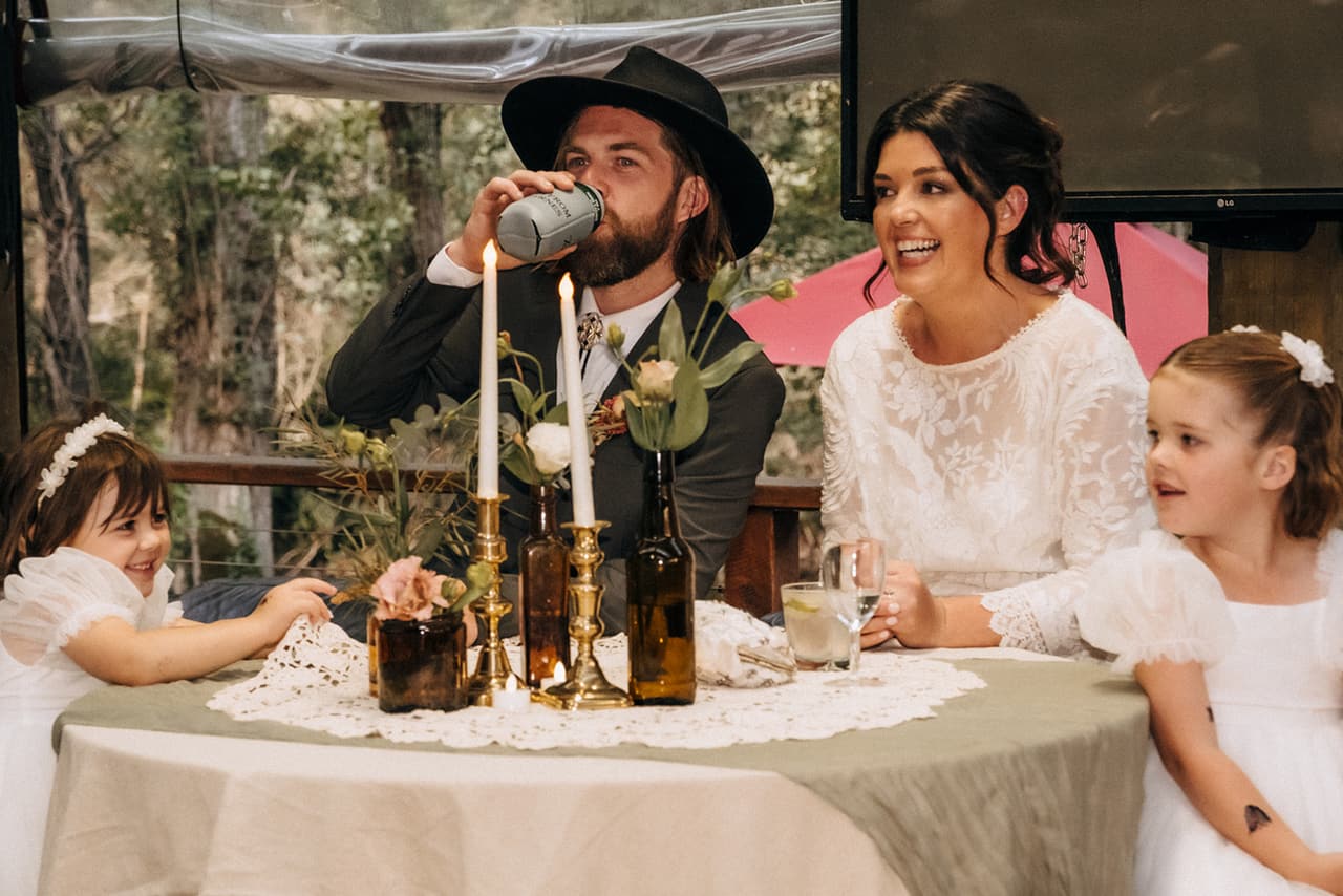 Todd skolling a drink at the bridal table as Lana and the two flower girls laugh