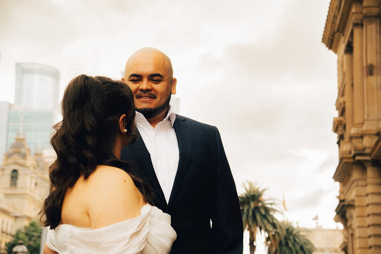 Diego smiling as Martina leans close to him, city towers and palm trees behind them