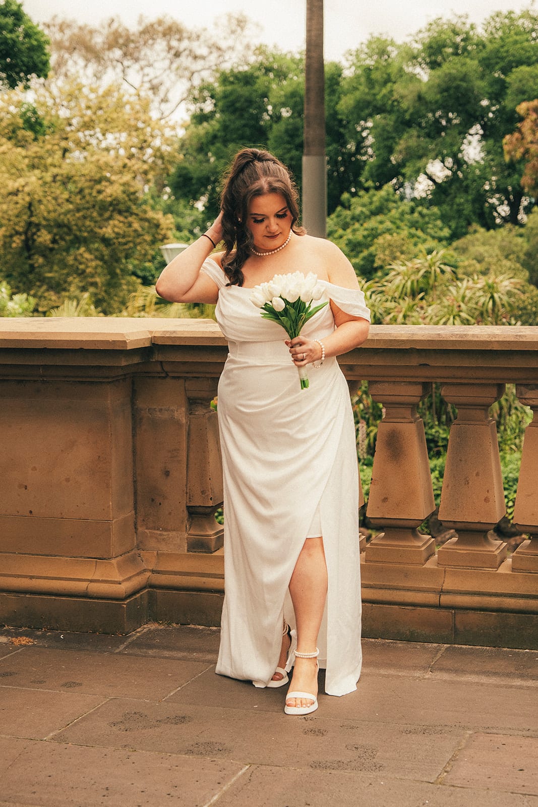 Martina laughing with a hand in her hair on the sandstone balcony of the Old Treasury Building, white tulips in her other hand