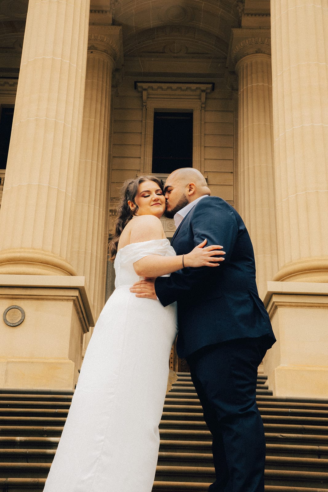 Diego kissing Martina’s cheek between the columns at the top of the Parliament House steps