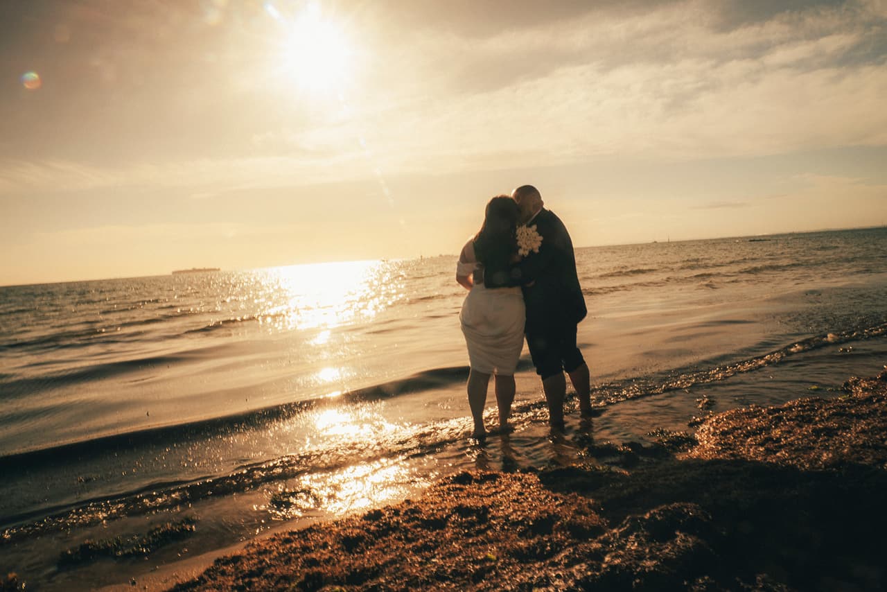 Martina and Diego in silhouette at the water's edge as the sun sets over the bay