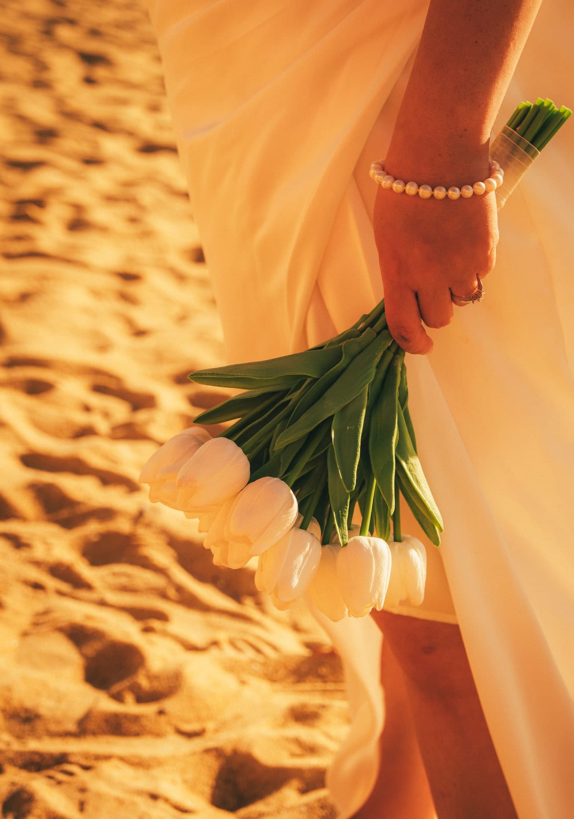 Close up of Martina’s white tulips and pearl bracelet against the sand