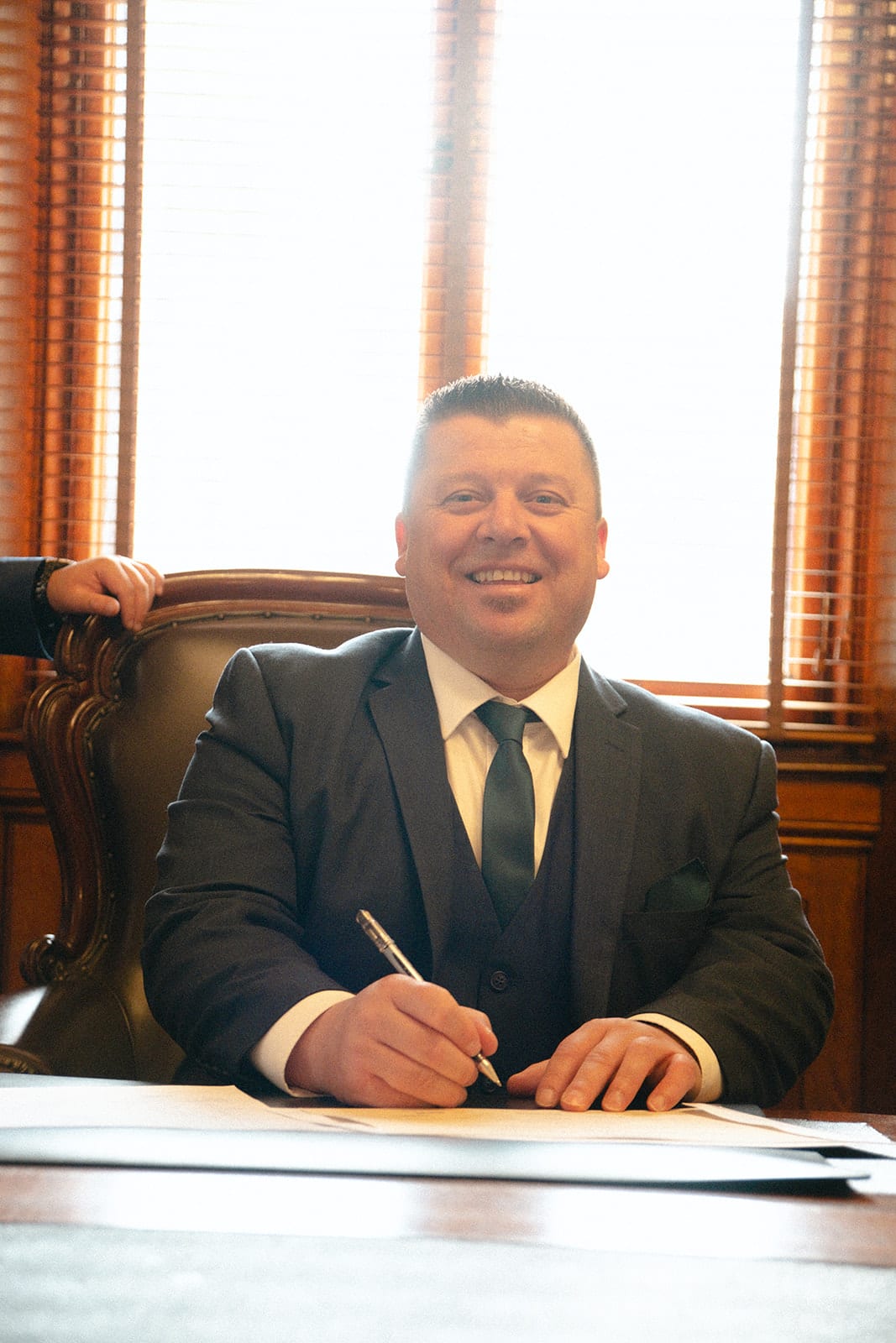 A witness in a suit and tie smiling as he signs at the registry desk