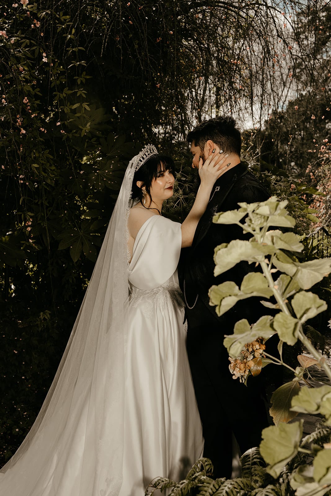 Porscha and Jordan close together in a dark corner of the garden, ferns and dried flowers around them