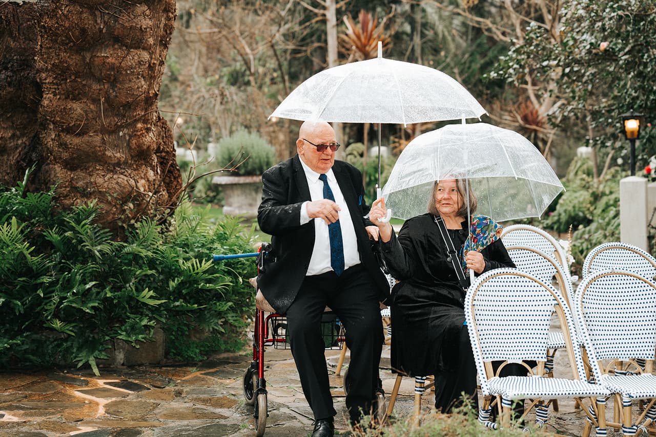 Guests sheltering under clear umbrellas as they take their seats by the chapel in the rain