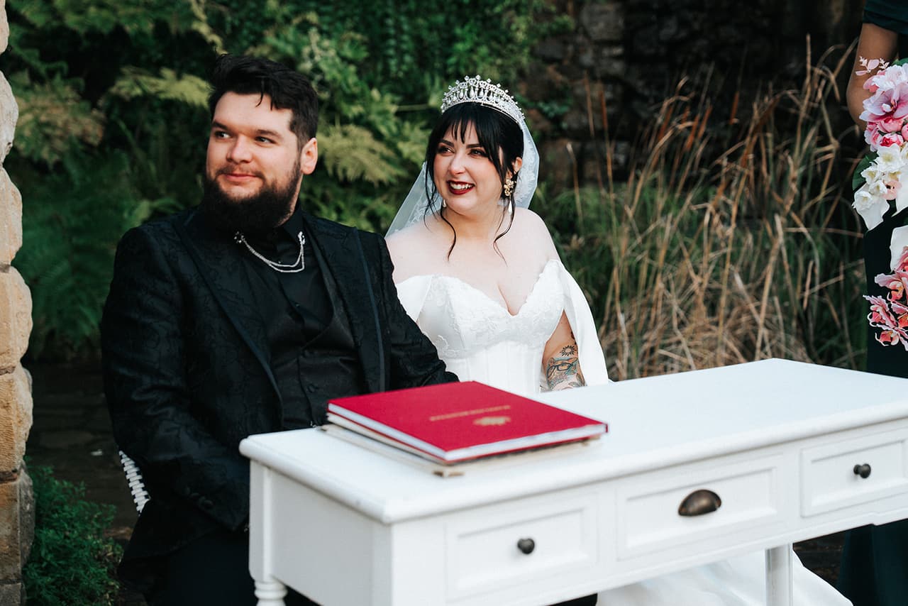 Porscha and Jordan smiling at a white desk as they sign the register