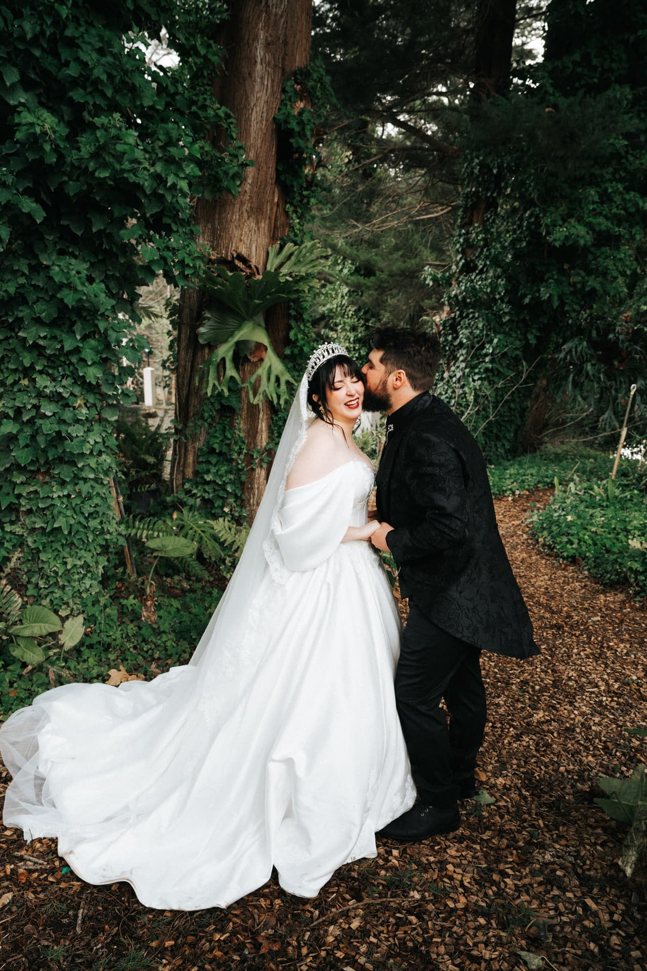 Jordan kissing Porscha’s cheek on a woodland path, her train spread across the leaves