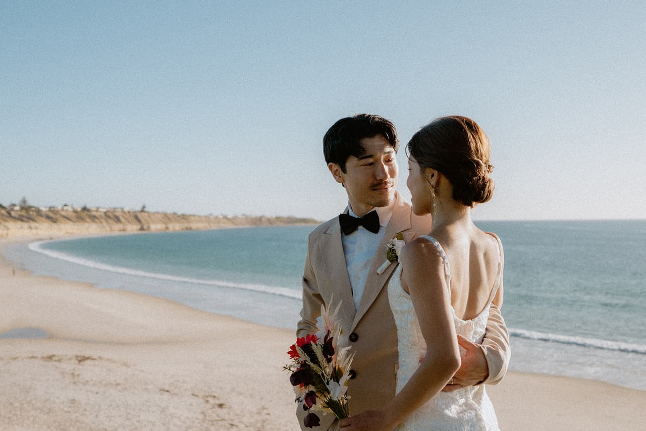 Shuto smiling at Sayuri on the clifftop, the long curve of the beach and the sea behind them