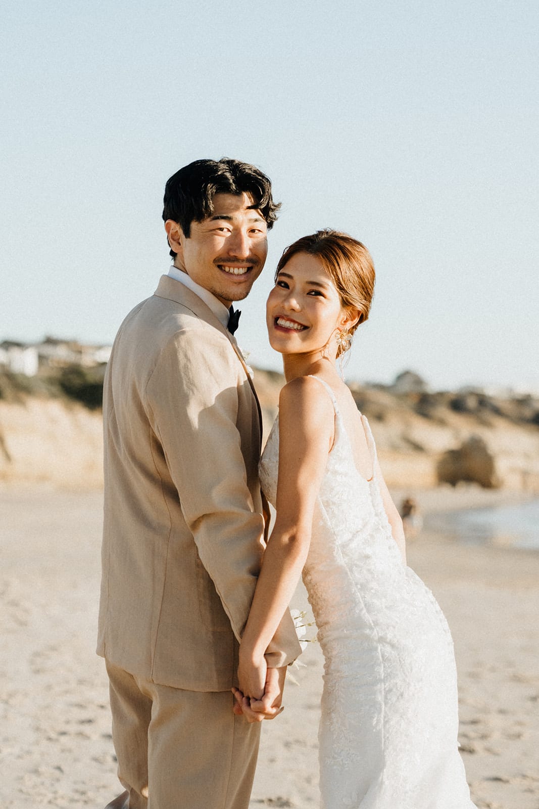 Shuto and Sayuri laughing towards the camera as they hold hands on the beach