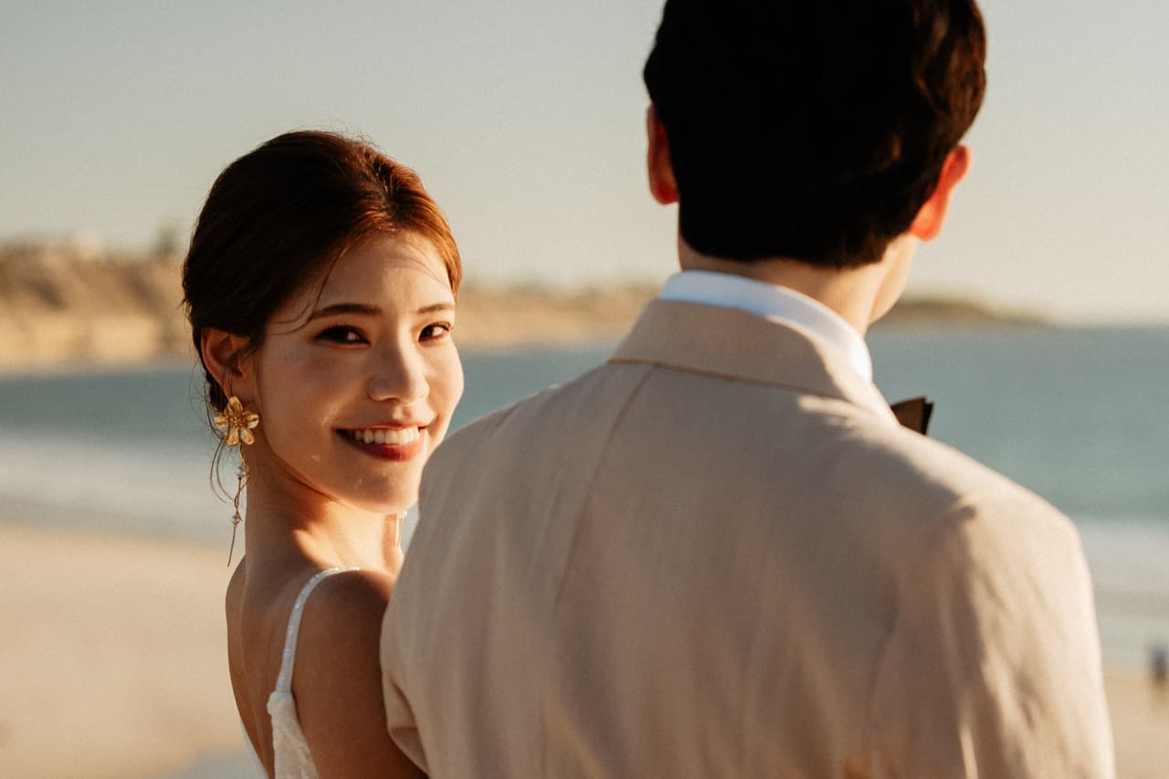 Close up of Sayuri smiling over her shoulder beside Shuto on the beach in late light