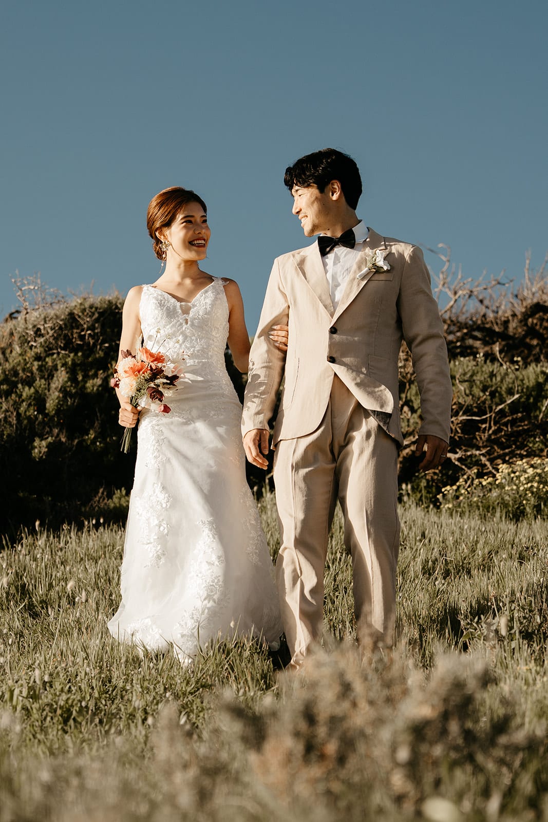 Sayuri laughing beside Shuto as they walk across the grassy clifftop under a clear blue sky