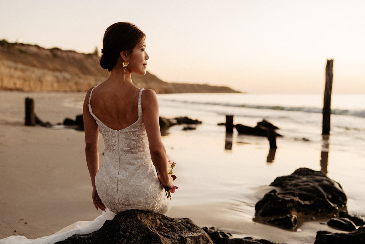 Sayuri sitting on a rock among the rock pools, looking along the beach towards the cliffs and the jetty posts