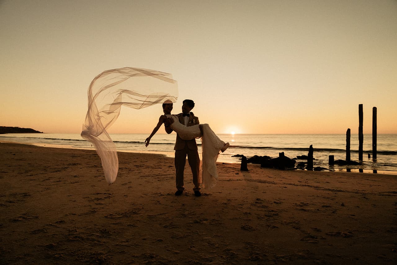 Shuto carrying Sayuri along the beach at sunset as her veil streams out in the wind