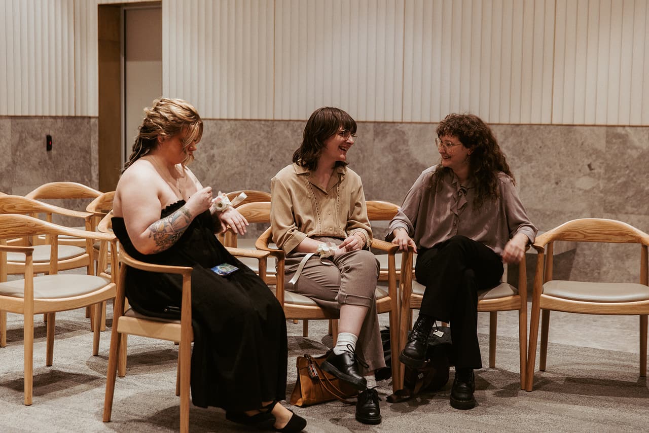 Three guests laughing together in the timber chairs as they wait for the ceremony