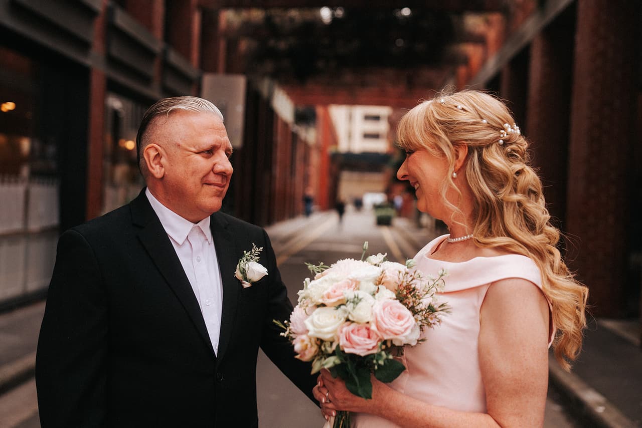 Jon smiling at Terrie as she laughs over her bouquet in a city laneway