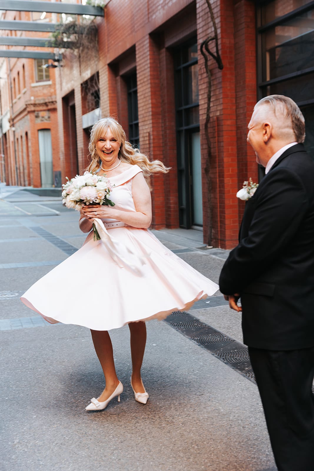 Terrie twirling her pink dress in the laneway outside the registry as Jon watches