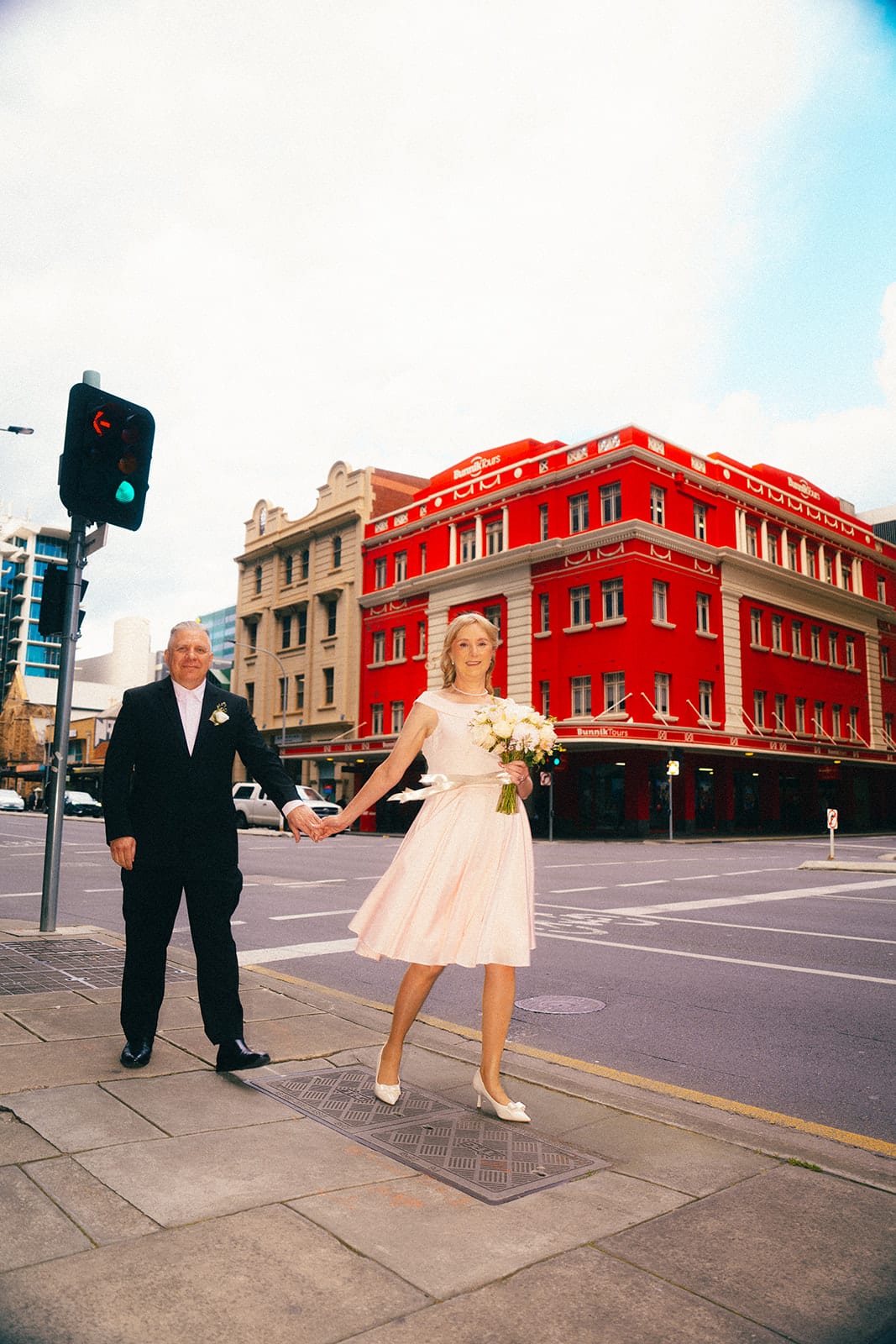 Terrie and Jon crossing the road in front of a bright red heritage building